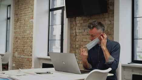 businessman puts on a face mask to work inside the office. mature male and woman practice social distancing.