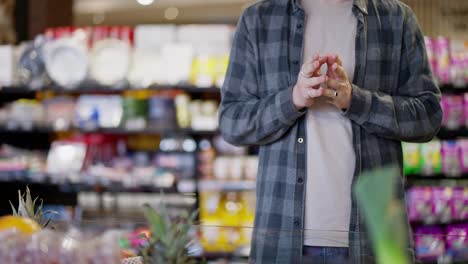 Close-up-of-a-supermarket-visitor-guy-in-a-plaid-shirt-rubbing-his-hands-while-choosing-goods-on-the-shelves-in-the-supermarket