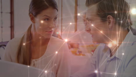 Woman and man collaborating on technology in office, with digital network overlay linking laptop
