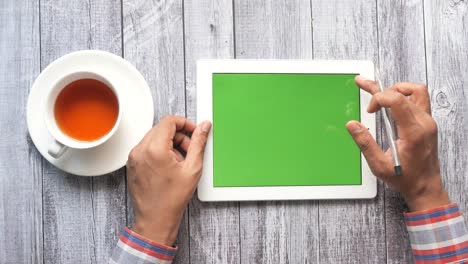 hombre usando una tableta con pantalla verde, bebiendo té en el escritorio