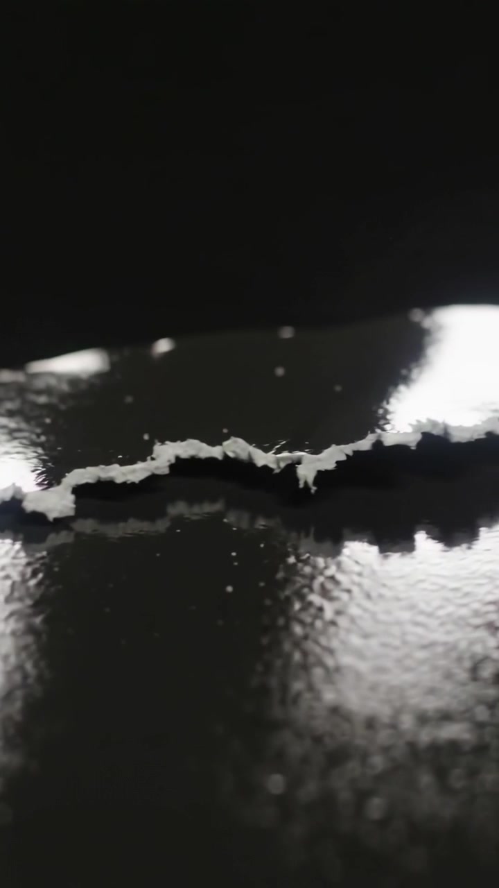 Video verticale: La telecamera zooma su una striscia bianca strappata in macro su sfondo nero, mostrando scaglie e luce dalla finestra.