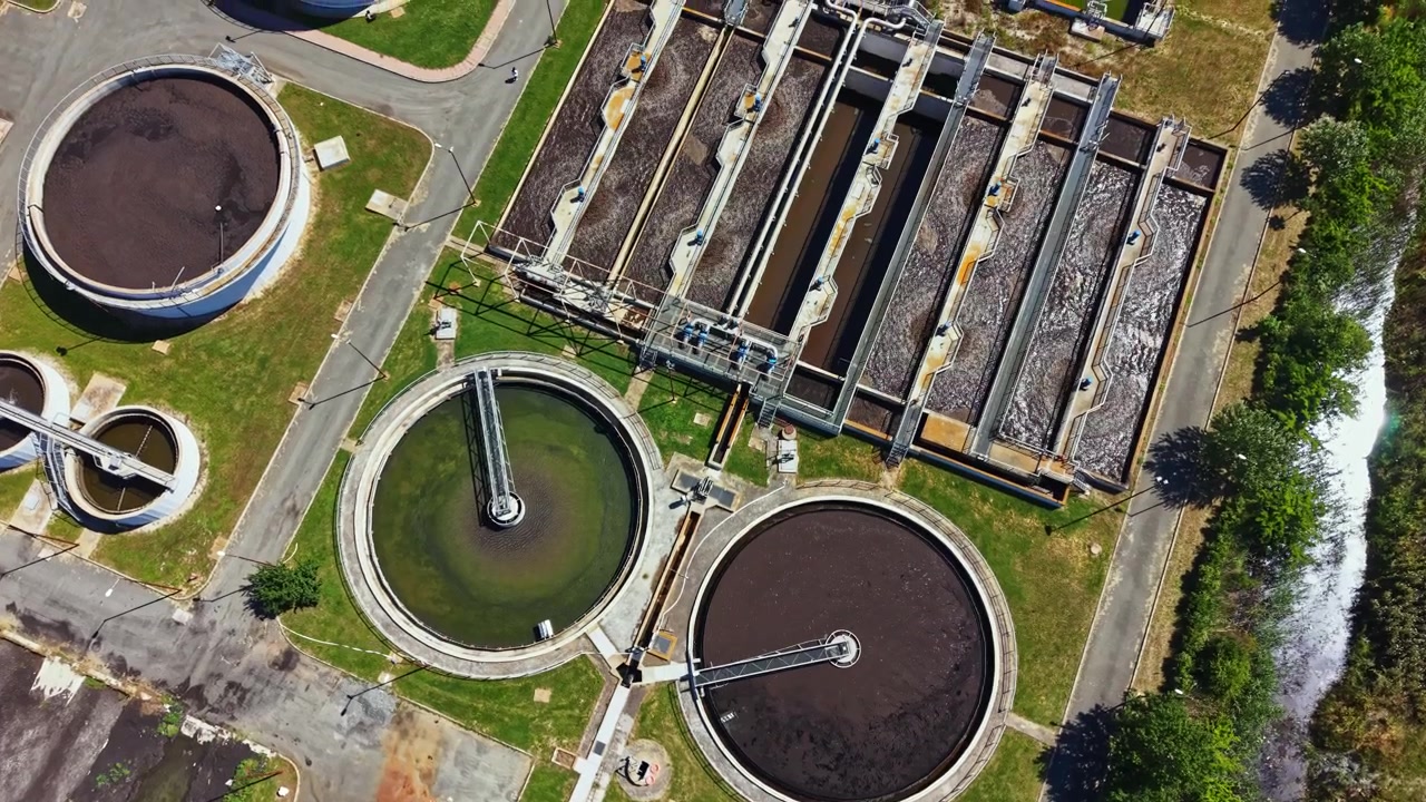 View of a wastewater treatment plant showing various tanks and processing equipment during a sunny day in a city