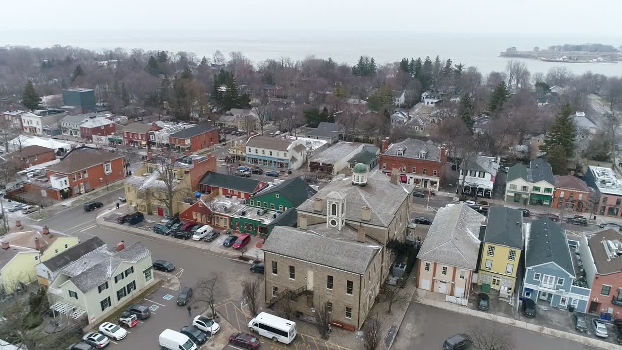 A drone captures an aerial view of Niagara-on-the-Lake's downtown courthouse, slowing zooming out on the surrounding historical buildings on a wintery day while snow lightly falls