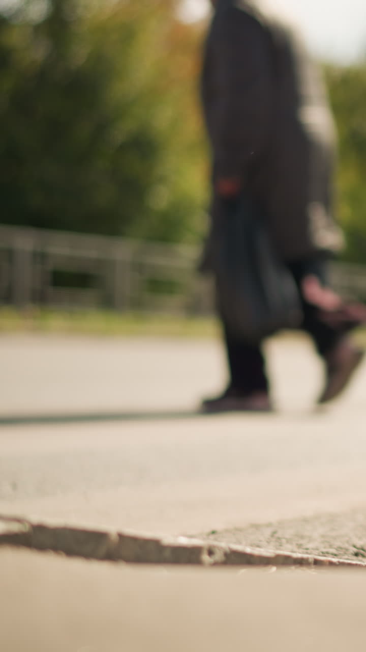 primo piano di piedi che attraversano le strisce pedonali con luce di metà mattina, diversi pedoni in movimento che mostrano scarpe e falcate varie, ombre e consistenza del marciapiede con messa a fuoco superficiale, atmosfera quotidiana da pendolari