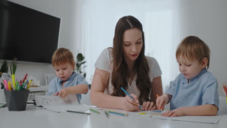 Una-Joven-Madre-Con-Dos-Hijos-Sentados-En-Una-Mesa-Blanca-Dibuja-Lápices-De-Colores-Sobre-Papel-En-Cámara-Lenta