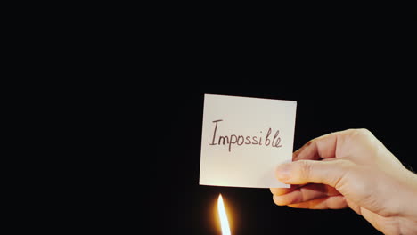 hand holds burning paper with inscription impossible