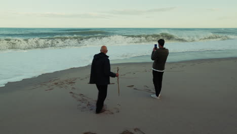 father and son watch the stormy ocean waves crash on the beach