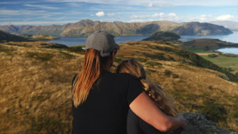 mother and daughter on hike enjoy new zealand landscape view, close-up pan from behind