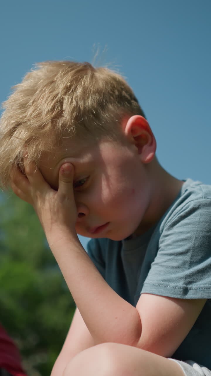 уставший маленький мальчик в синей рубашке потирает лицо левой рукой, с размытым взглядом на своего старшего брата, смотрящего на него.