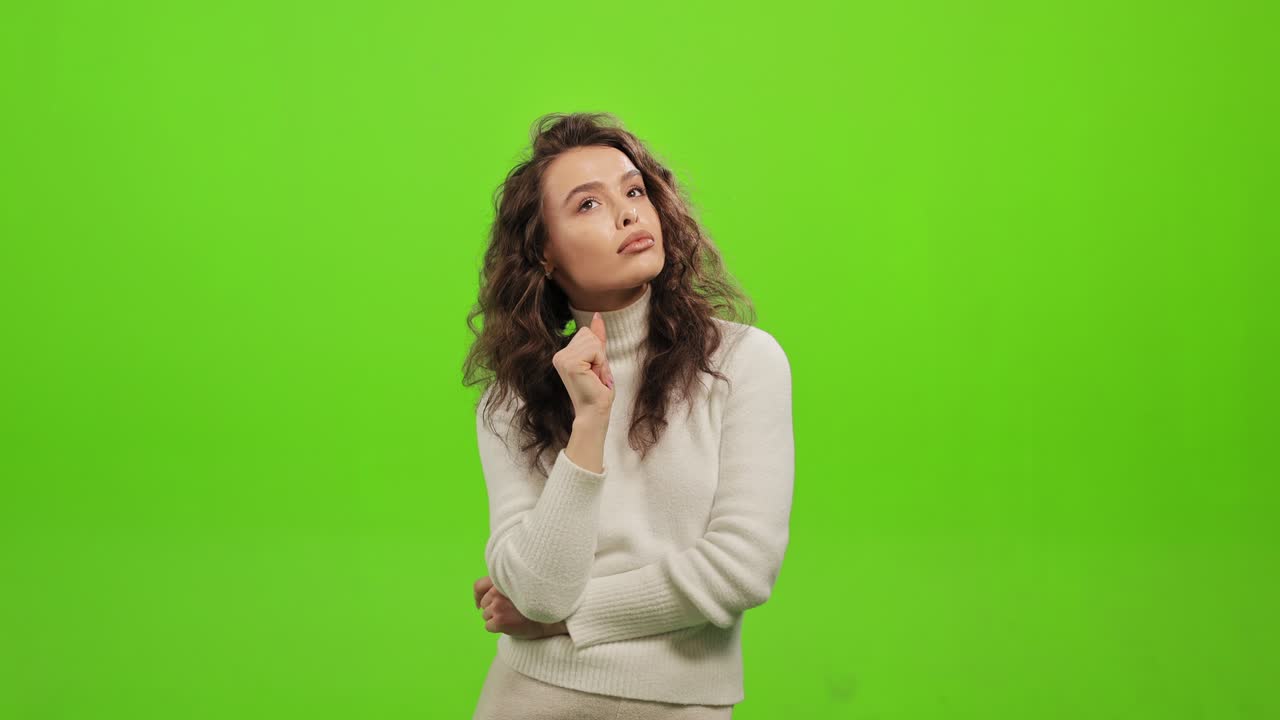 la mujer está de pie y pensando. ella está sosteniendo su mano a su barbilla. ella está de pie en un fondo verde. pantalla verde. 4k.