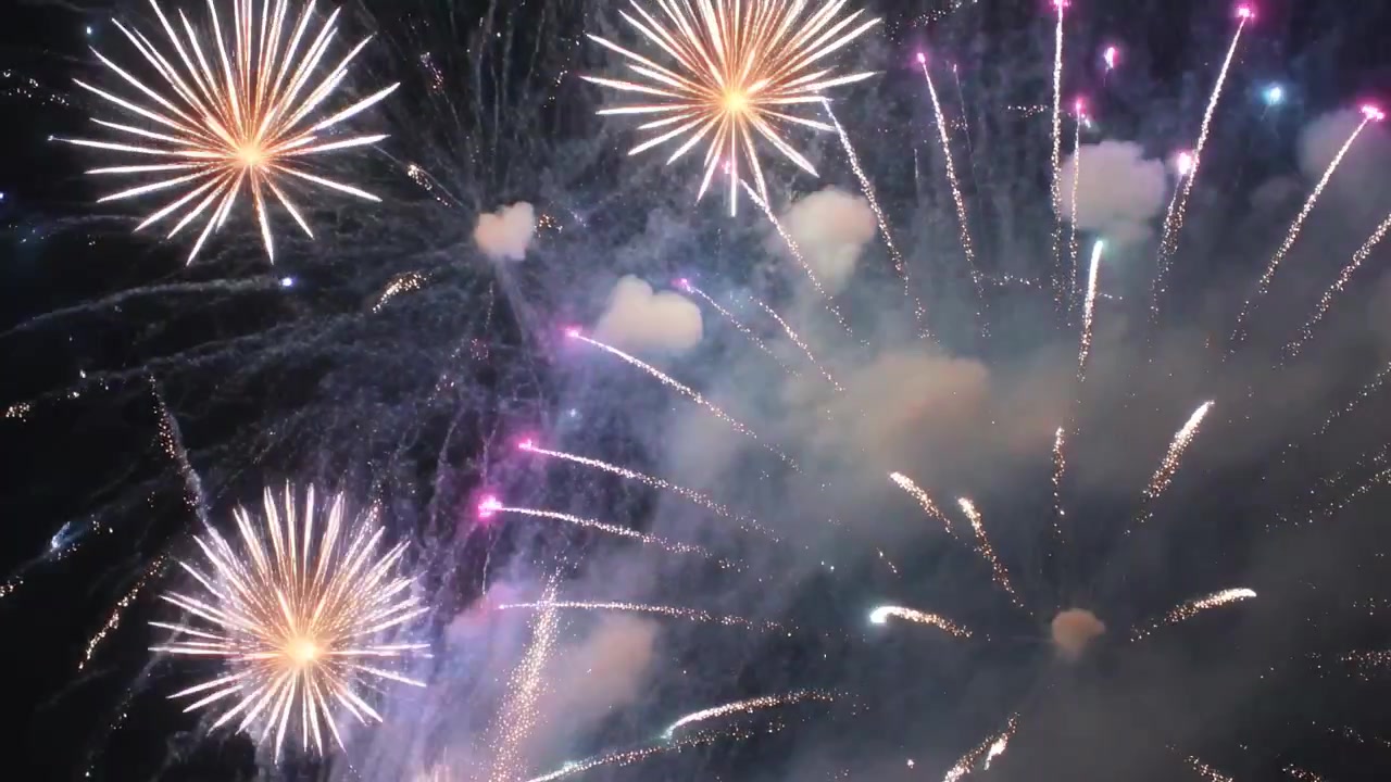 Detonazione di fuochi d'artificio che creano esplosioni a stella nel cielo notturno aperto per una celebrazione, con foschia di fumo.