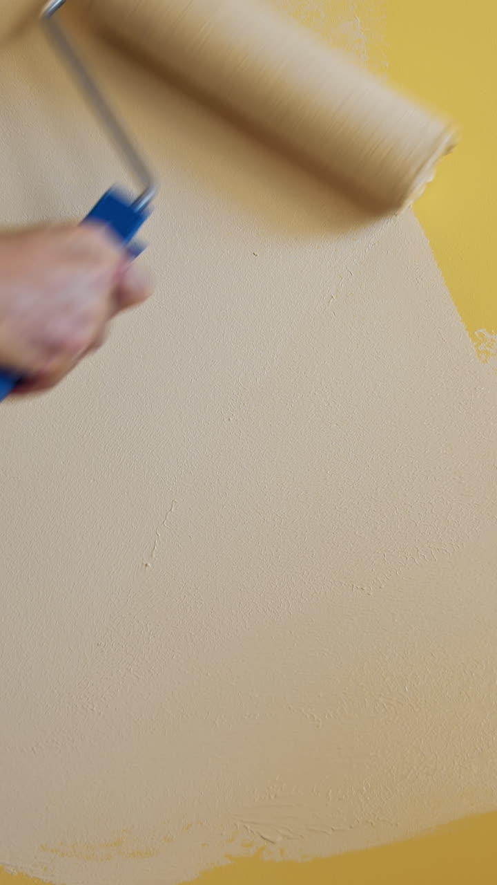 Roller painting yellow wall with creamy paint. Hand of a worker doing renovation the room with light color. Close-up. Makeover concept. Vertical video