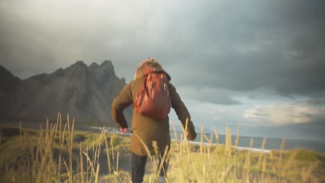 hiker running through grassy dunes on a beach in front of a rocky mountain landscape