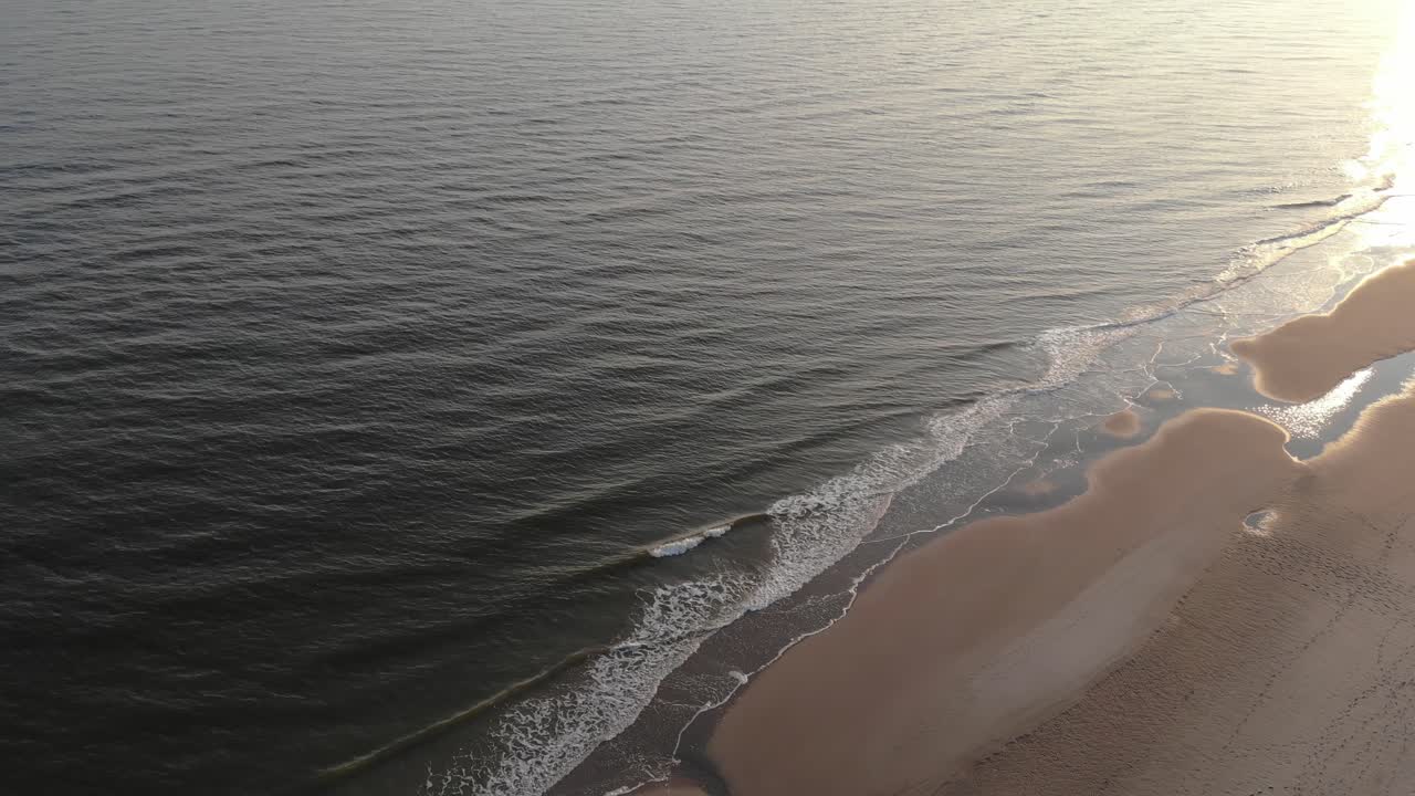 Aerial, pan, drone shot overlooking calm waves hitting a beach, at sunset, on Langeoog island, in North Germany