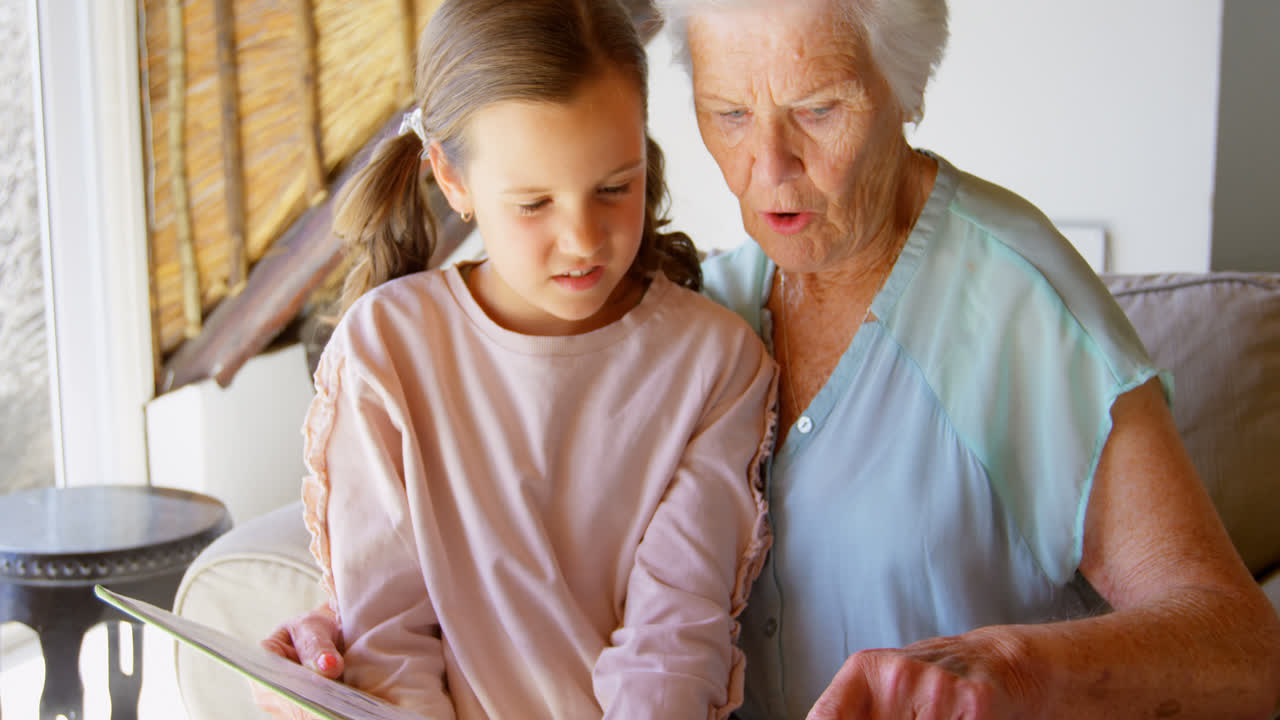 vista frontal de la abuela y la nieta caucásicas mirando el álbum de fotos 4k