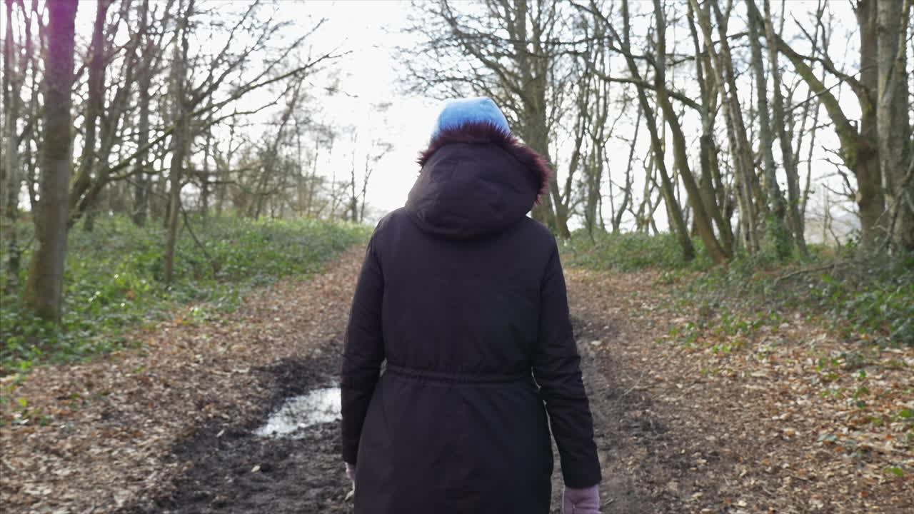 A woman walking through the woods on a footpath. SLOW MOTION GIMBAL SHOT FROM HIGH TO LOW.