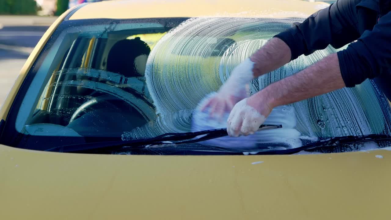 Washing yellow car windscreen with blue mitt and lots of shampoo suds