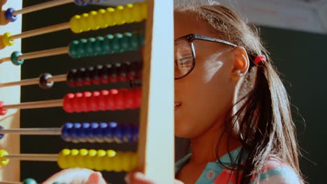 Side-view-of-African-American-schoolgirl-with-spectacle-learning-math-with-abacus-in-classroom-4k