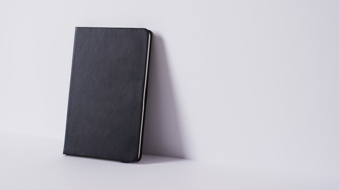 Close up of closed black book leaning on wall with copy space on white background in slow motion
