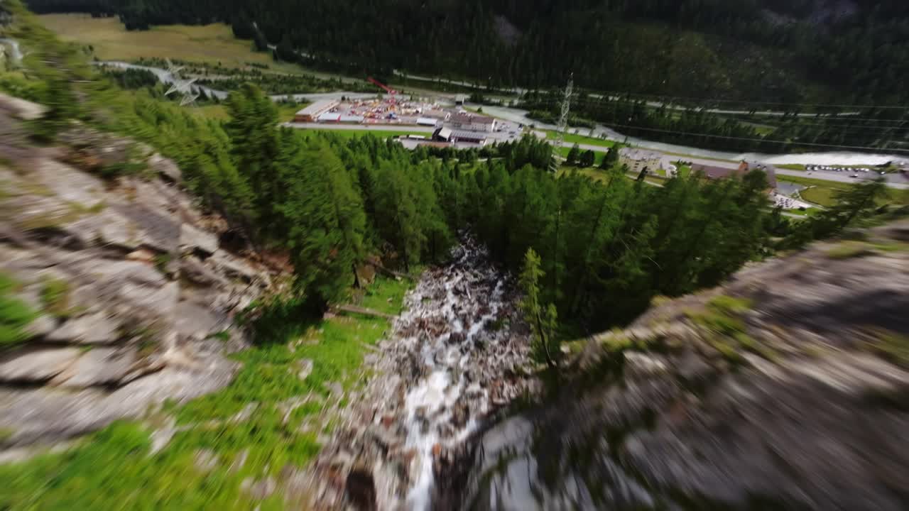FPV drone dives along a Swiss mountain waterfall, plunging close to the rocks before tilting up to gain height and continuing the descent from above the cascade