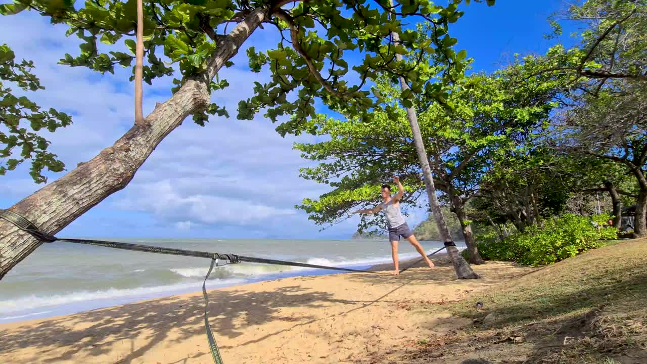 macho adulto joven practicando en slackline en trinity beach en cairns