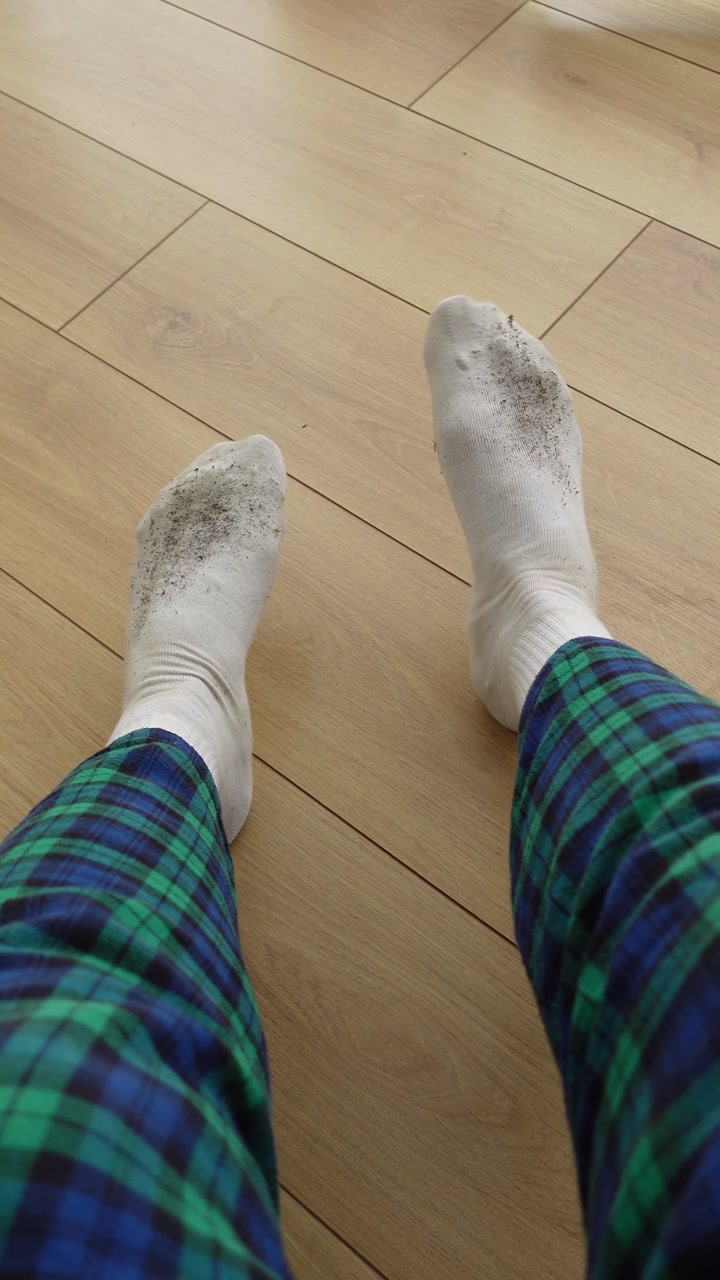 Dirty White Socks on Feet Wearing Plaid Pajamas on Wooden Floor