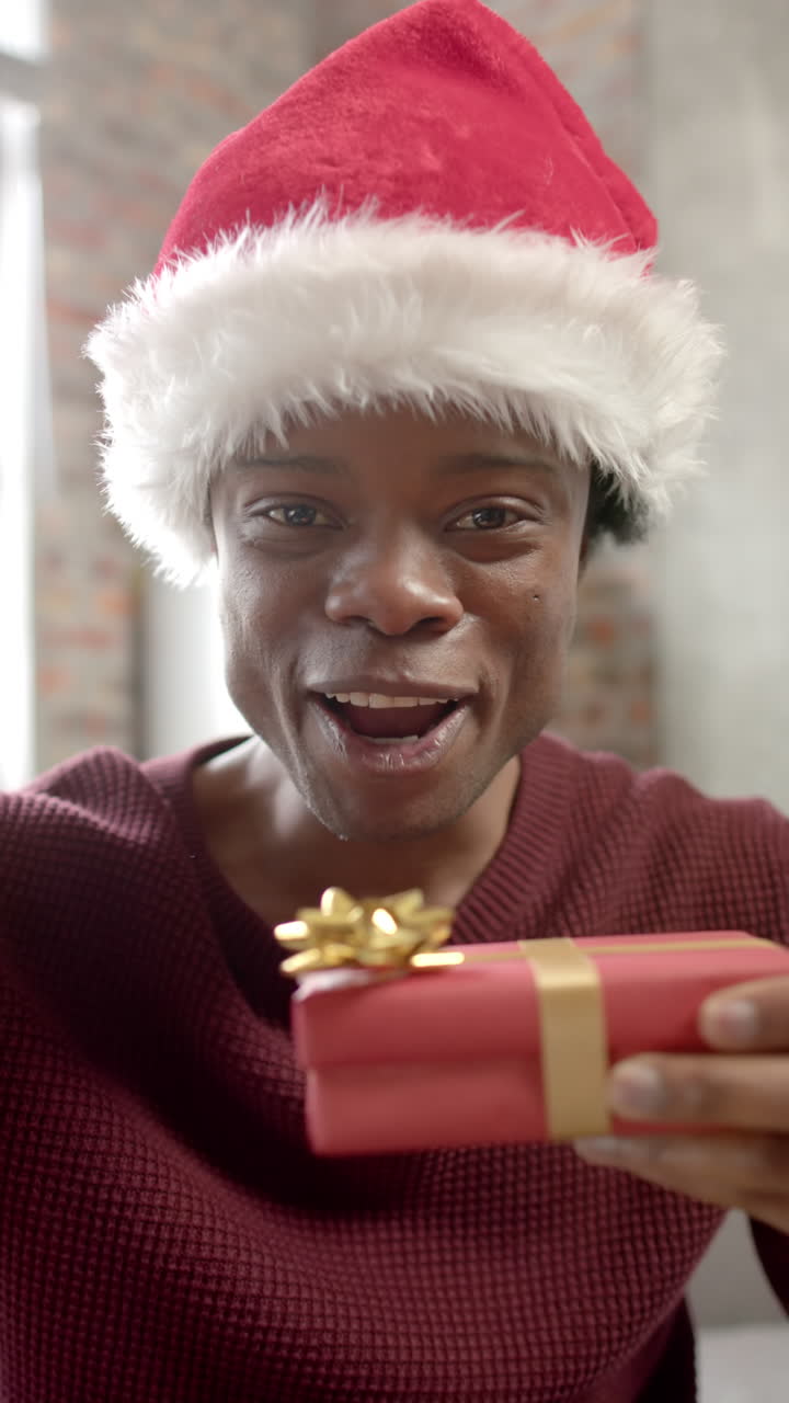 Vertical video of african american man wearing santa hat having video call at home, slow motion