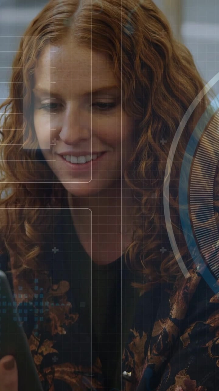 Vertical video: Woman tapping tablet and lowering gaze showing HUD panels and smiling at tech feed