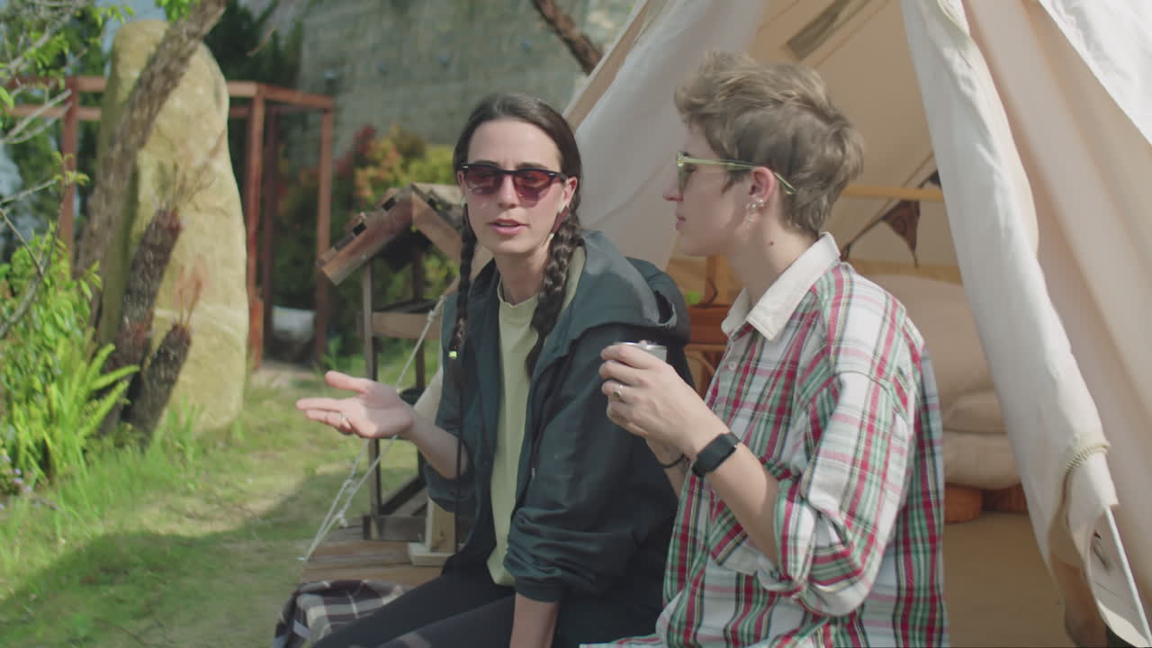 Two Girlfriends Sitting at Glampsite and Talking over Tea