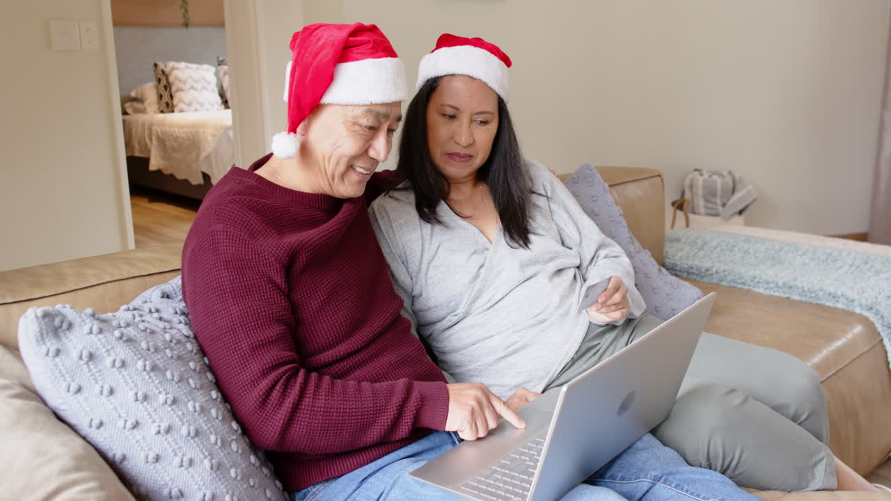 Christmas time, Senior asian couple wearing Santa hats shopping online with laptop at home