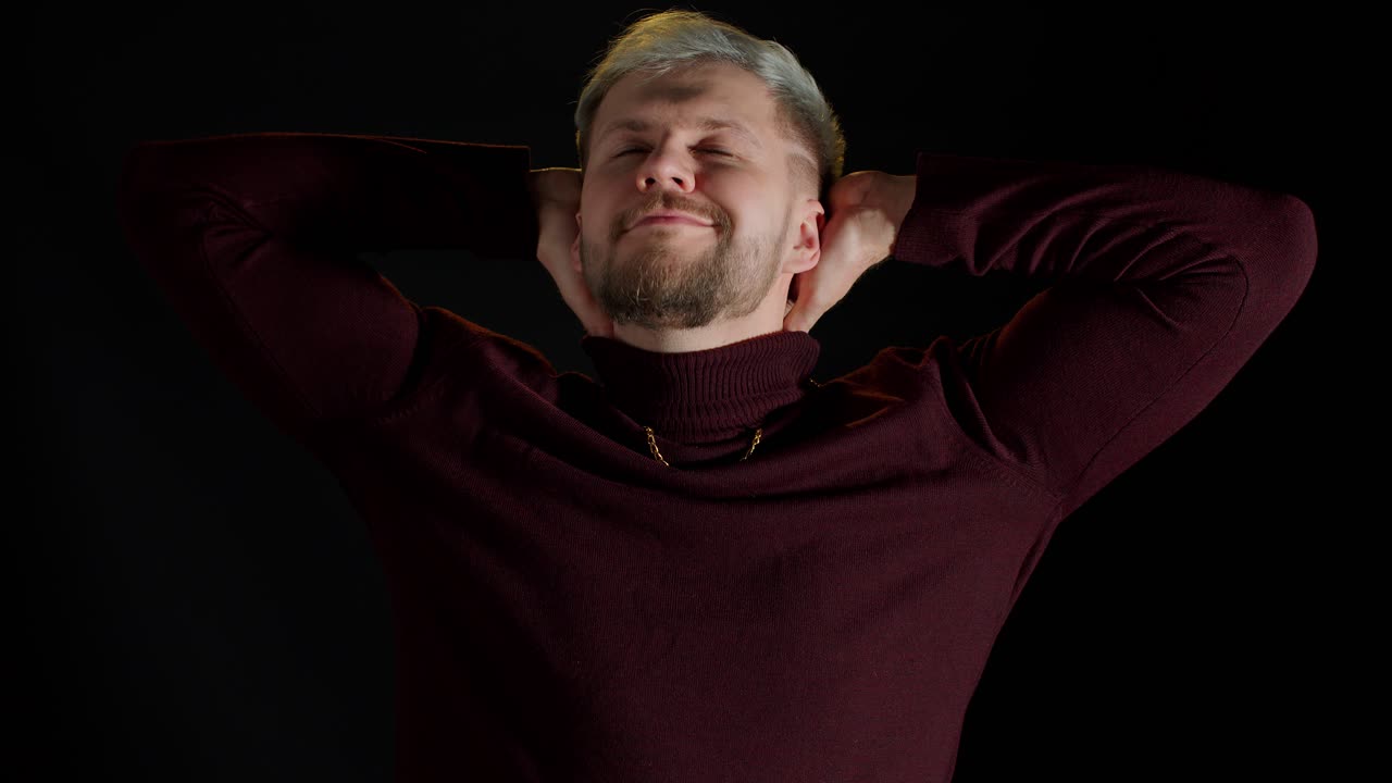 joven sonriente y alegre con las manos cruzadas sobre la cabeza, mirando a la cámara, fondo negro