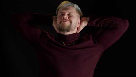 Smiling-cheerful-young-man-holding-hands-crossed-over-head,-looking-at-camera,-black-background