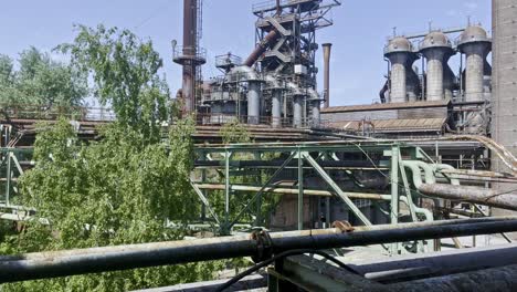 Vista-Aérea-Sobre-Viejas-Tuberías-Y-Cables-Oxidados-De-Una-Fábrica-Histórica-Que-Está-Siendo-Reclamada-Por-La-Naturaleza-En-El-Parque-Paisajístico-En-Duisburg-Al-Norte-De-Alemania