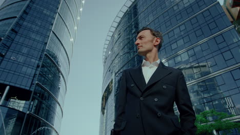 handsome caucasian man in suit standing outdoors looking around at finance district, low angle view