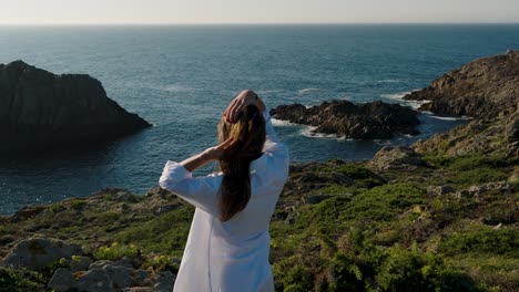 Woman-Brushing-Hair-With-Hands-While-Overviewing-Seascape-Near-Ferrol-In-Galicia,-Spain