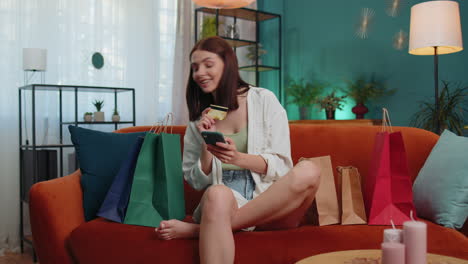 Happy-shopaholic-young-woman-sitting-with-shopping-bags-making-online-payment-with-credit-card