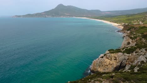 Scenic-natural-rocky-coast-beach-sandy-bay-on-the-tourist-holiday-island-Sardinia,-Italy,-with-mountains-and-sun,-clear-blue-turquoise-and-calm-water-close-to-Costa-Rei