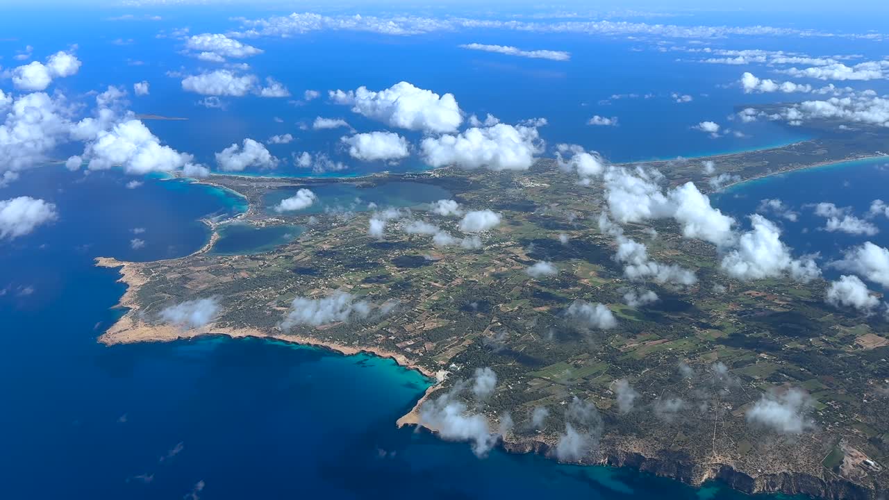 An elevated spining right side aerial view of Formentera island recorded from an airplane cockpit in a summer morning, with few low cloiuds. Handeld camera cockpit shot
