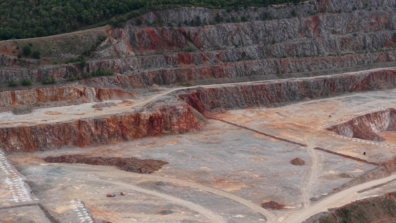 An aerial perspective shows a large open pit quarry with exposed rock strata, illustrating industrial resource extraction and geological formations.