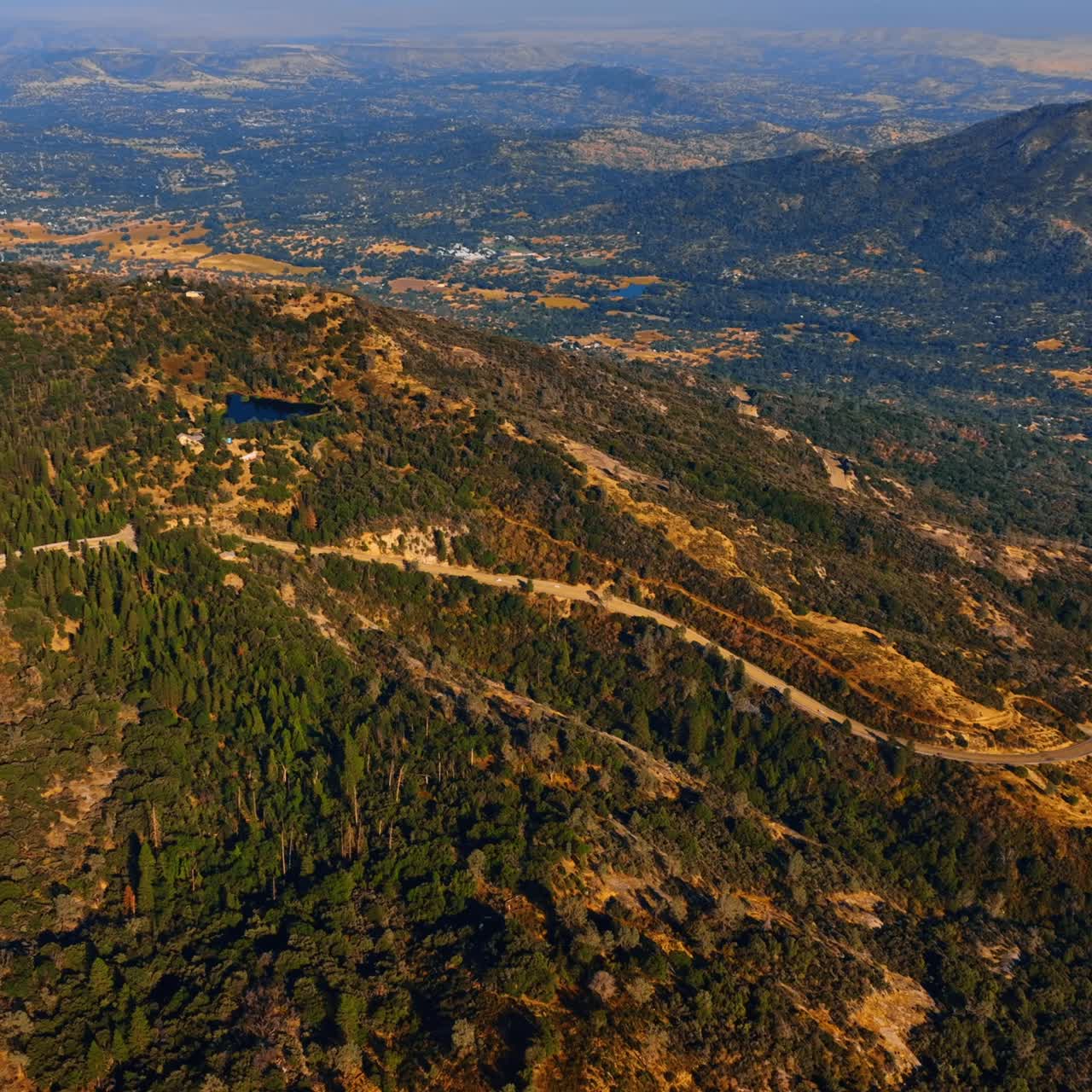 Four lane road crossing the mountains. Sunny view of the Sierra National Forest in USA from aerial perspective