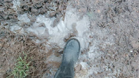 Looking-down-at-someone-wearing-boots-cracking-an-icy-puddle,-handheld