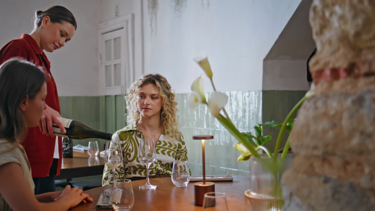 Girls enjoy friendly gathering at restaurant. Woman waitress pouring wine