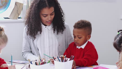 millennial female infant school teacher sitting at table in class working with a boy, front view