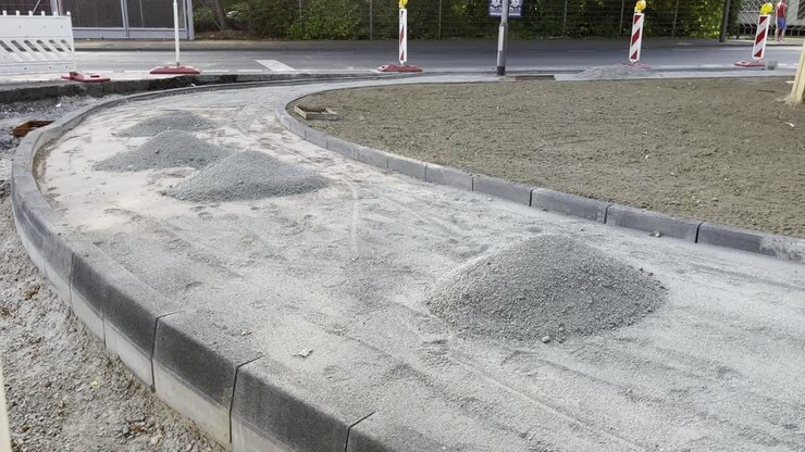 Street sidewalk is being built with small piles of stones and path border with construction site