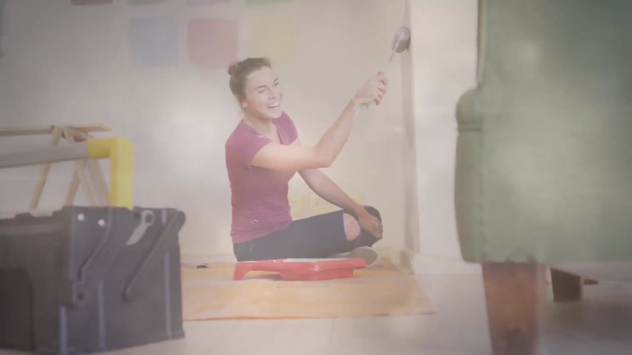 punto de luz contra la mujer caucásica pintando su pared mientras su gato camina en casa