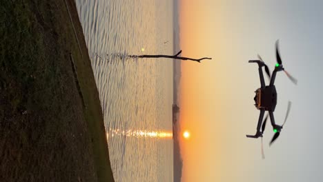 Vertical-view-of-a-small-consumer-drone-hovering-stationary-filming-the-sunset-in-Thailand