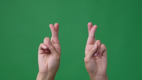 hands with fingers crossed over green screen