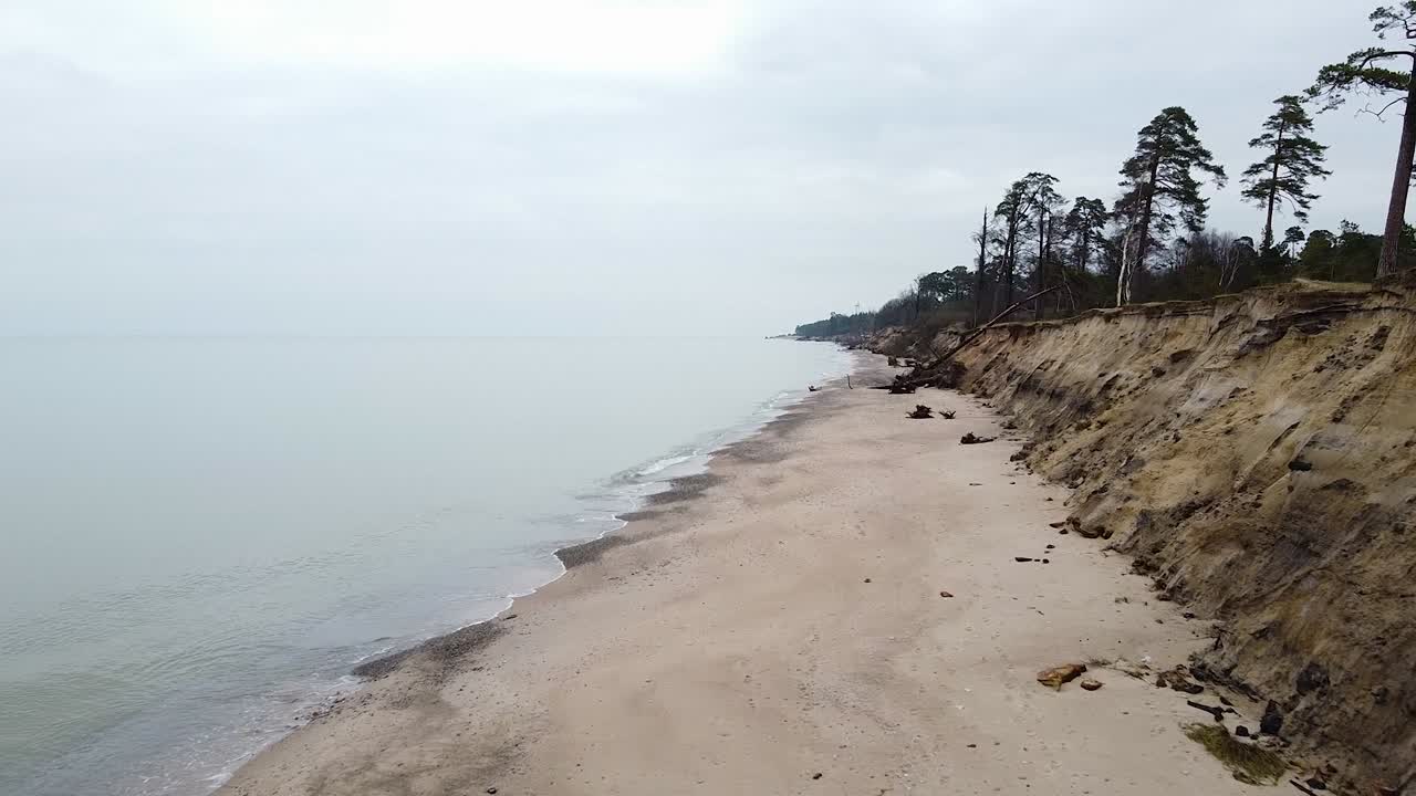 Aerial view of Baltic sea coast in overcast spring day, steep seashore dunes damaged by waves, coastal erosion, climate changes, drone shot moving forward
