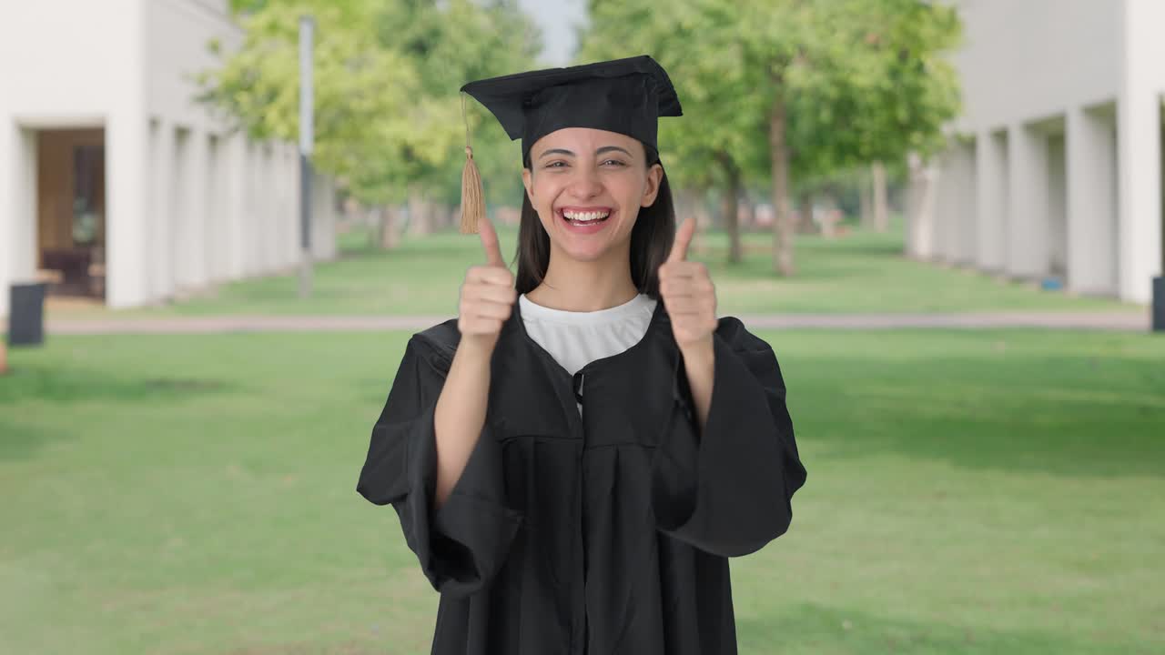 feliz chica graduada de la universidad india mostrando los pulgares hacia arriba