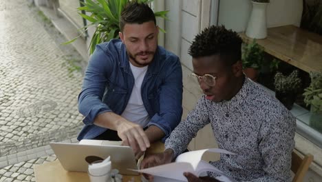 Freelancers-using-laptop-and-looking-at-papers-in-cafe